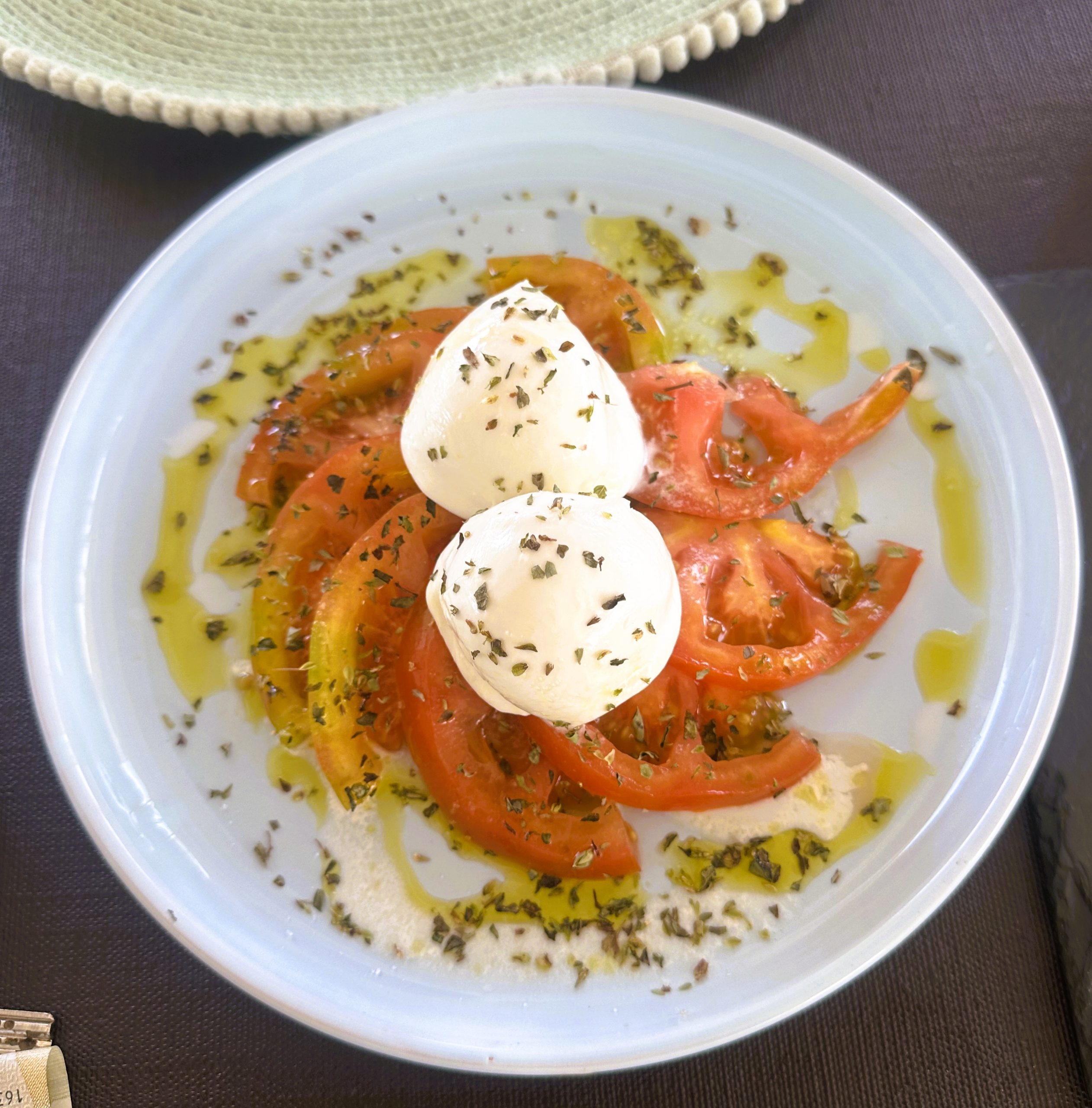 A plate of burrata, sliced tomatoes, olive oil, and dried herbs, all high quality ingredients.