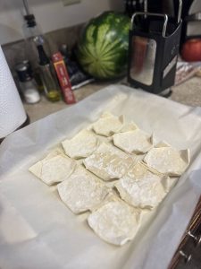 Raw puff pastry sheet cut into nine squares with edges lined up on a parchment-lined baking sheet